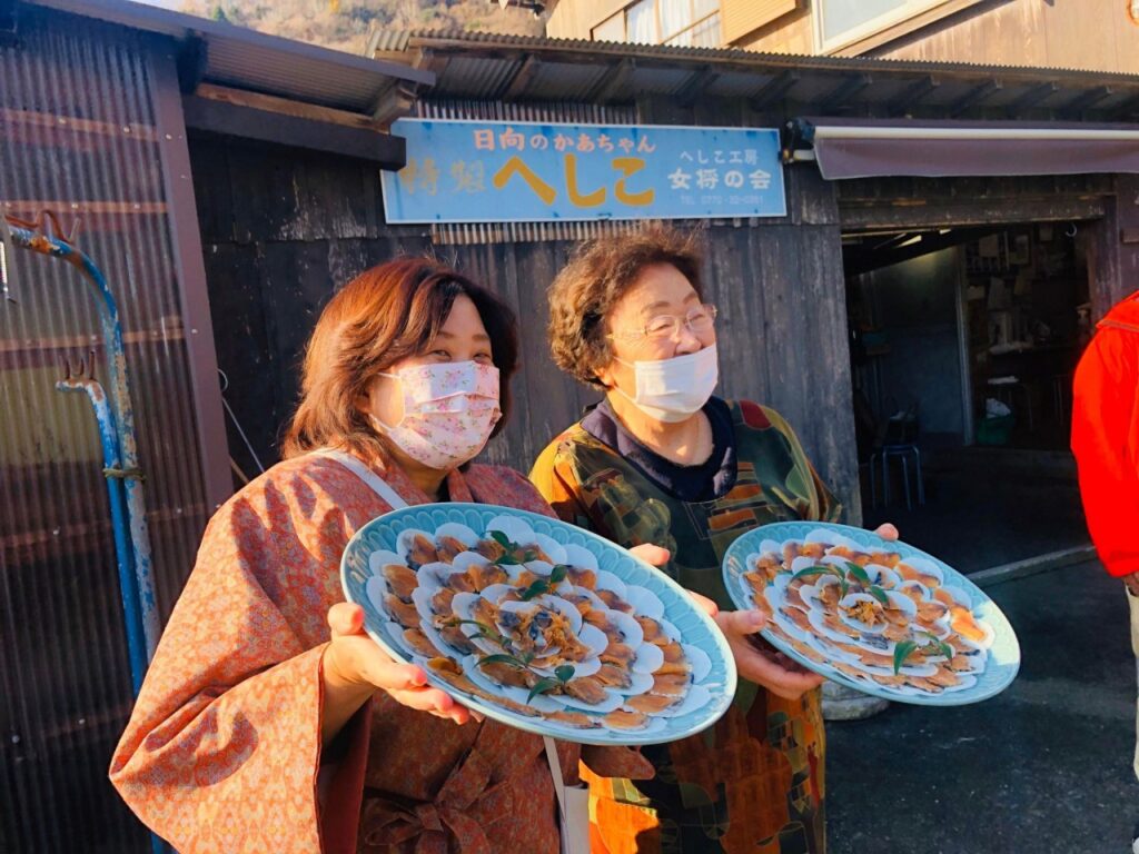 へしこの生産者と特製へしこ（サバの糠漬け）の写真。生産者が大皿に盛り付けたへしこを持って笑顔を見せている様子。