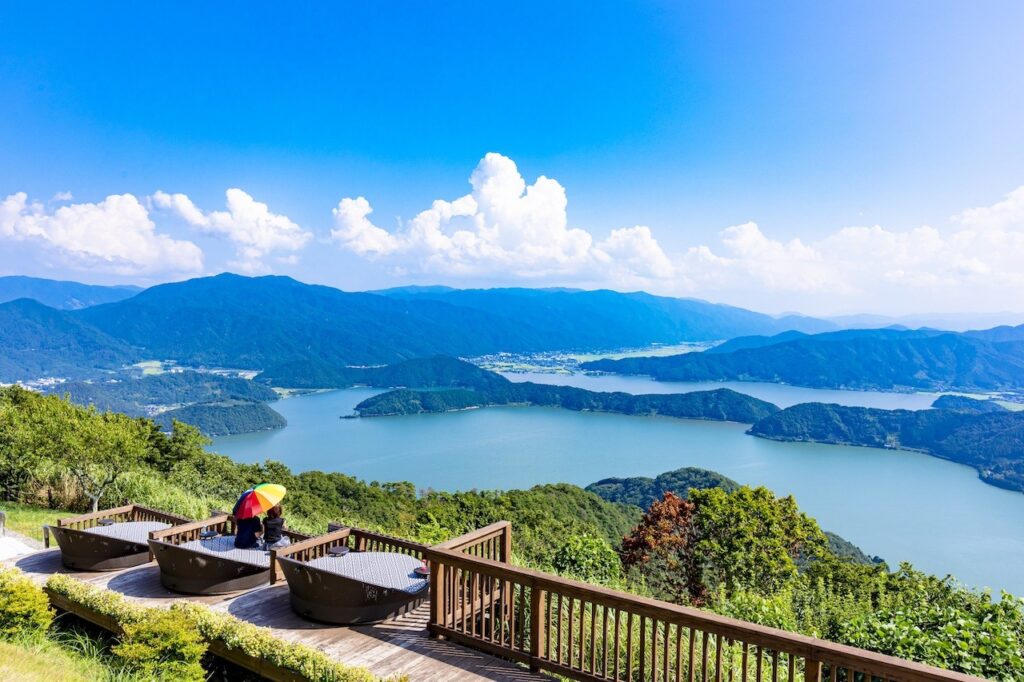 レインボーライン山頂公園からの絶景。福井県美浜町と若狭町にまたがる三方五湖を見渡すパノラマビューが広がり、晴天の青空の下、自然の美しさが楽しめる。