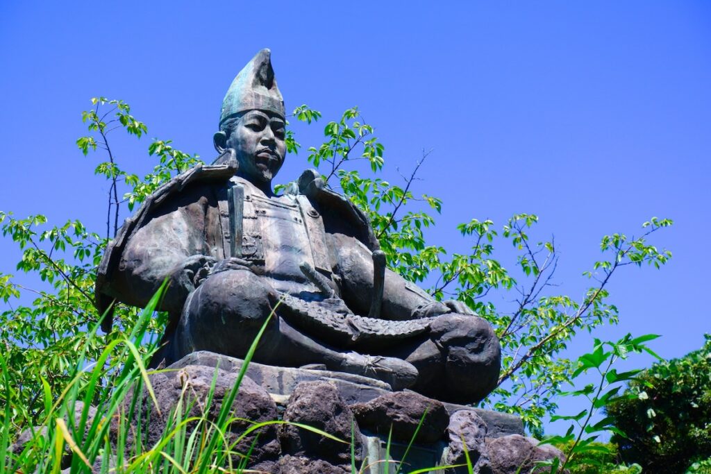 鎌倉市の源氏山公園にある鎌倉幕府初代将軍・源頼朝の座像。緑豊かな風景と青空を背景に静かにたたずんでいる。