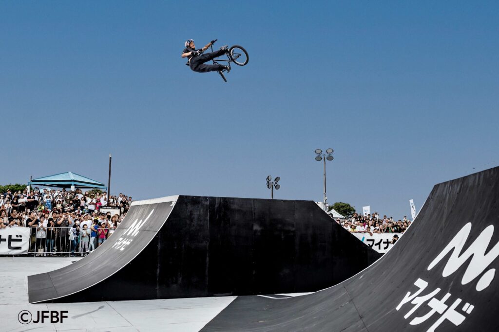 Nakamura, a BMX rider, performing an aerial trick at the Mynavi Japan Cup BMX Freestyle event. Spectators watch the impressive mid-air stunt at the 2023 competition in Yokosuka City.